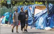  ?? Francine Orr Los Angeles Times ?? A WOMAN walks her children past an encampment near Larchmont Charter School-Selma in Hollywood.