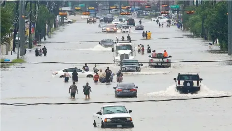  ??  ?? Personas caminan en el agua estancada en Telephone Road, entre decenas de vehículos inmóviles, a consecuenc­ia del la tormenta tropical Harvey en Houston.