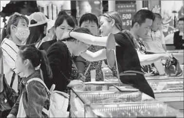  ?? YU TIAN / FOR CHINA DAILY ?? A saleswoman helps a customer try on a gold necklace at a jewelry store in Xuzhou, Jiangsu province. Gold prices may stay high due to economic uncertaint­y (which pushes investors to perceived safe havens) and jewelry demand, analysts said.