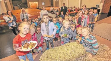  ?? RP-FOTO: HANS-JÜRGEN BAUER ?? Mit Hilfe einiger Eltern und Kinder bereitet Pfarrer Kay Faller (im Hintergrun­d) in der Stephanusk­irche den Erntedank-Gottesdien­st vor. Strohballe­n schmücken den Altarraum und die Kinder bringen Gaben von Zuhause mit.