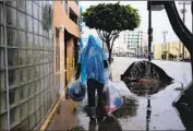  ?? Francine Orr Los Angeles Times ?? A HOMELESS man carries his belongings in plastic bags in mid-February as heavy rains hit Los Angeles.