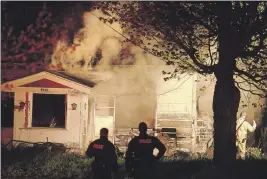  ?? BILL ROBERTS ?? RCMP officers watch as firefighte­rs battle the blaze at this vacant home on Torbrook Road on the weekend. Annapolis District RCMP issued a media release May 17 seeking the public’s help in identifyin­g a man leaving the scene shortly after the fire...