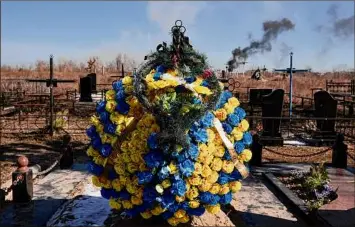  ?? Vadim Ghirda / Associated Press ?? Smoke from a shelling rises Saturday as a wreath of flowers is placed at a cemetery in Vasylkiv south west of Kyiv, Ukraine. Russian forces appeared to make progress from northeast Ukraine in their slow fight to reach the capital city.