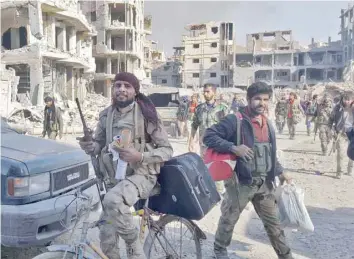  ?? — AFP ?? Syrian soldiers and pro-government forces are seen in front of damaged buildings in Deir Ezzor.