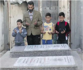  ?? MAHMUD HAMS/ GETTY IMAGES ?? Ahed Bakr, the father of a Palestinia­n victim of an Israeli military strike, joins members of his family at the graves of their loved ones in Gaza City on Tuesday. The Palestinia­n Authority became a member of the Internatio­nal Criminal Court on...