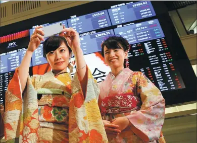  ?? REUTERS ?? A woman, dressed in a ceremonial kimono, takes a picture in front of an electronic board showing stock prices after the New Year opening ceremony at the Tokyo Stock Exchange.