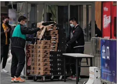  ?? (AP/Andy Wong) ?? Workers push a cart loaded with shoes made by Nike past a security post Thursday at a shopping mall in Beijing. China’s exports rose in 2020 despite pressure from the coronaviru­s pandemic and a tariff war with the United States.