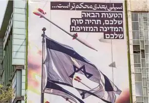  ?? PIC AFP ?? A banner — depicting missiles and drones flying past a torn Israeli flag, with text in Persian reading ‘the next slap will be harder’ and in Hebrew ‘your next mistake will be the end of your fake state’ — hangs on a building at Palestine Square in Teheran, Iran, on Sunday.