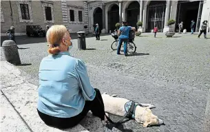  ?? VINCENZO PINTO AFP/GETTY IMAGES ?? A woman and her dog pause outside Rome's Santa Maria in Trastevere square on Sunday during the country's lockdown. Parks and public gardens are set to reopen on Monday.