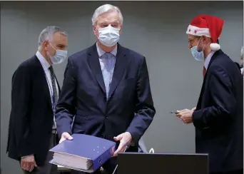  ?? OLIVIER HOSLET VIA AP ?? A colleague wears a Christmas hat as European Union chief negotiator Michel Barnier, center, carries a binder of the Brexit trade deal during a special meeting of Coreper, at the European Council building in Brussels, Friday, Dec. 25, 2020.