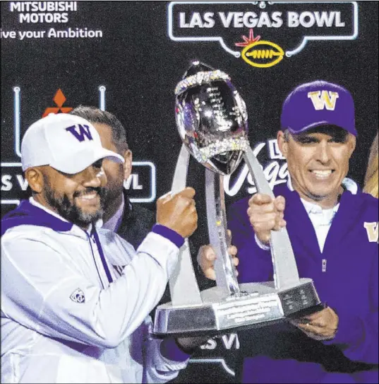  ?? L.E. Baskow Las Vegas Review-Journal @Left_Eye_Images ?? Defensive coordinato­r-turned-incoming head coach Jimmy Lake, left, joins retiring Washington Huskies head coach Chris Petersen in displaying the Las Vegas Bowl trophy after the Huskies overwhelme­d No. 18 Boise State 38-7 on Saturday at Sam Boyd Stadium.