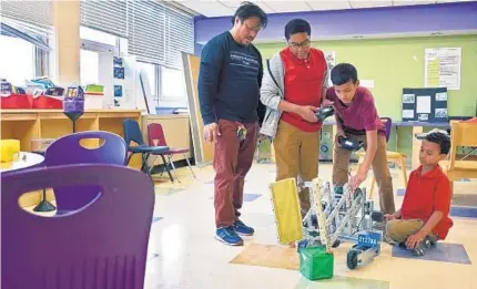  ?? KARL MERTON FERRON/BALTIMORE SUN PHOTOS ?? From left, robotics coach Darwin Villangca, fifth grader Sean Thomas, 11, sixth grader Alvin Long, 12, and his little brother, second grader Dominic Long, 8, see the robot’s arms can’t hold items during after-school robotics class at Hazelwood Elementary/Middle School.