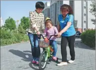  ?? LU YING / XINHUA ?? Liu and Xiao Ding help another foster child learn to ride a bicycle at their residentia­l community.