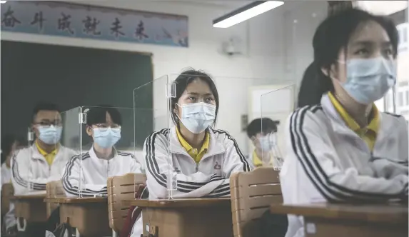  ?? GETTY IMAGES ?? Senior students sit in a Wuhan classroom with transparen­t boards placed around each desk to separate people as a precaution­ary measure against COVID-19.