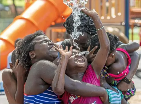  ?? Steph Chambers/Post-Gazette ?? Evelyn Niyosaba, 6, holds on to her friend Grace Barry, 6, as water is dumped onto them and their friends in 90-degree weather Tuesday at Mellon Spray Park in Shadyside.