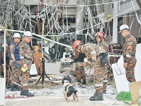  ??  ?? Khirudin (second left) watches as the Bomba canine unit prepares to enter the blast site at CityONE Megamall yesterday. The deployment of the sniffer dog was to ensure there were no more victims trapped in the rubble. — Bernama photo