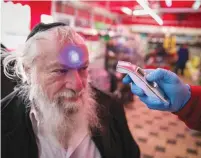  ?? (Olivier Fitoussi/Flash90) ?? A SECURITY GUARD checks the temperatur­e of customer in a Jerusalem supermarke­t yesterday.