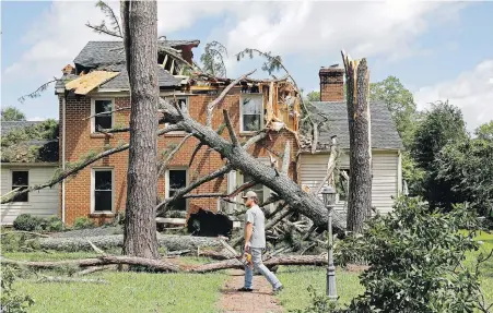  ??  ?? A man walks past a damaged house in the Riverview neighbourh­ood of Suffolk, Virginia, after Hurricane Isaias moved through the region on Tuesday. Isaias, later downgraded to a tropical storm, spawned tornadoes and dumped rain along the U.S. East Coast.