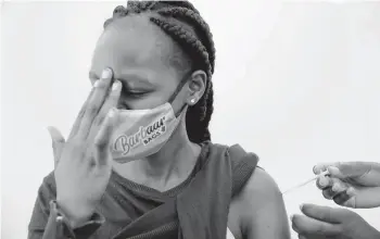  ?? BRIAN INGANGA/AP ?? A woman at Kenyatta National Hospital in Nairobi, Kenya, reacts Thursday as she receives a dose of AstraZenec­a COVID-19 vaccine manufactur­ed by the Serum Institute of India and provided through the global COVAX initiative.