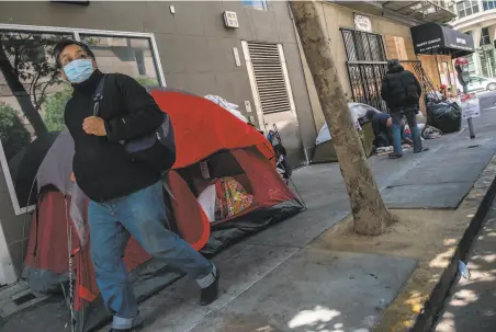  ?? Photos by Nick Otto / Special to The Chronicle ?? A pedestrian walks past a small tent encampment on the sidewalk near the corner of Taylor and Ellis streets in the Tenderloin.