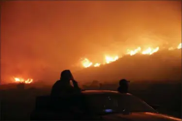  ?? JAE C. HONG — THE ASSOCIATED PRESS ?? Two spectators watch as a wildfire burns along the 101 Freeway Tuesday in Ventura Raked by ferocious Santa Ana winds, explosive wildfires northwest of Los Angeles and in the city’s foothills burned a psychiatri­c hospital and scores of homes and other...