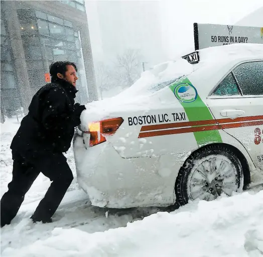  ?? PHOTO AFP ?? Dans les rues de Boston ensevelies par au moins 30 centimètre­s de neige, un homme a aidé ce taxi incapable d’avancer.