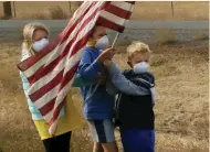  ?? (Leah Millis/Reuters) ?? CHILDREN WAVE the American flag on Saturday while wearing masks to protect them from smoke as the motorcade of US President Donald Trump passes in Paradise, California.