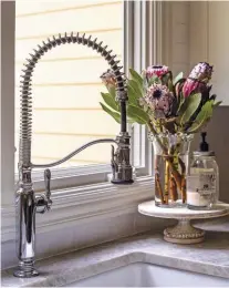  ??  ?? |ABOVE| LIGHT PLAY. A classy chrome faucet in the middle of the dark cabinets and stunning countertop­s adds a timeless feel to the kitchen. Lauren says, “The best part about the sink is that it’s positioned under a window that overlooks Bobbi’s garden. The sunlight just dances off the chrome faucet.” Lauren believes that chrome is the ultimate metal to mix into kitchen designs because it looks amazing with everything, almost like diamonds!