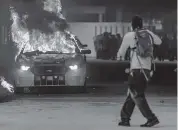  ?? MATIAS J. OCNER mocner@miamiheral­d.com ?? A protester passes a police car on fire in downtown Miami on Saturday night.