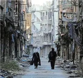  ?? /Reuters ?? Dire situation: Women walk past damaged buildings at the Yarmouk Palestinia­n refugee camp on the southern outskirts of Damascus.