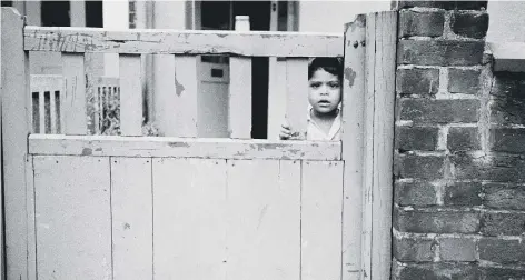  ??  ?? A young Zaroob peers through the gate in Cromwell Road, Peterborou­gh, in 1980.