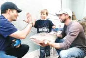  ?? PHOTO BY SHELLEY MAYS/THE TENNESSEAN ?? Caleb Daniel, 5, of Franklin, Tenn., high-fives Predators catfish thrower Tom Dennis, as Little’s Fish Market owner Chris Little shows Daniel the catfish he will help throw onto the ice before the Predators’ home game tonight.