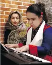  ??  ?? Melika Aghaei, 14, with Down syndrome plays piano, while Aylin Agahi — founder of Downtism Cafe and a musician — listens.