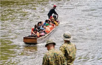  ?? Arnulfo Franco/Associated Press ?? Panamanian police stand on the banks of the Chucunaque River on Friday while migrants head north after walking across the Darién Gap from Colombia.