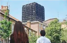  ?? AFP ?? The burnt-out shell of the Grenfell Tower block is seen behind terraced houses as local residents look on in North Kensington, West London.