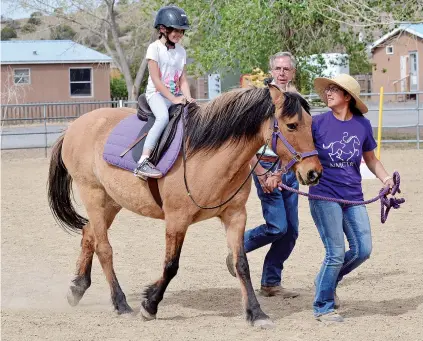  ?? PHOTOS BY ELAYNE LOWE/THE NEW MEXICAN ?? Demi Padilla rides Maggie last week at New Mexico Center for Therapeuti­c Riding as part of her Adaptable Curriculum Education class at the New Mexico School for the Deaf. Ashley Armijo, director of the center, guides Maggie in a trot along with a...