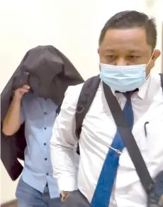 ??  ?? Mohd Hizan covering his face after court proceeding­s yesterday. Also seen is his lawyer Mohd Ari.