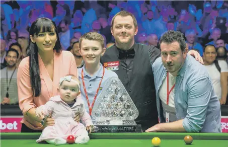  ??  ?? Mark Allen celebrates with his family, and with the trophy, after winning the 2018 Dafabet Masterstit­le yesterday.