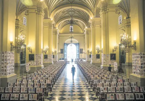  ?? AP ?? A man walks among portraits of people who died due to the COVID-19, inside the Cathedral in Lima, Peru, on Saturday.