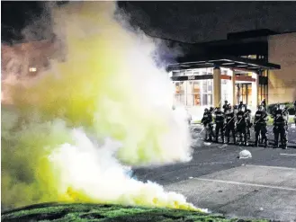  ?? REUTERS ?? Tear gas is seen Sunday night as officers stand guard outside Brooklyn Center Police Department with trash thrown at them by demonstrat­ors at their feet, after police allegedly shot and killed a Black man earlier in the day in Brooklyn Center, Minn.