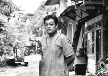  ??  ?? A resident displays a photograph showing the previous condition of the Tongkol kampung in Jakarta before residents made changes to improve the environmen­t. Brightly coloured brick and wooden houses line a clean riverside path amid trees and vegetable...