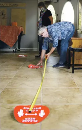  ?? JOEL ROSENBAUM — THE REPORTER ?? Vacaville Museum staff member Heidi Casebolt uses a measuring tape to allow her to place placards on the floor six feet apart informing visitors to maintain proper social distance while viewing the exhibits. The museum is set to open Thursday with limited capacity and masks required for both visitors and staff.