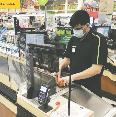  ?? JONATHAN HAYWARD/ THE CANADIAN PRESS ?? A clear barrier helps shield a cashier from potential exposure to the coronaviru­s at a grocery store in North Vancouver, B.C.