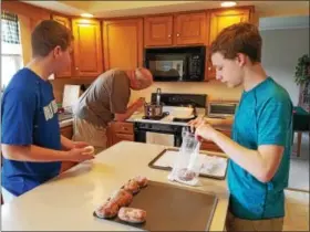  ??  ?? Rob Good, center, checks to see if it’s time to flip the fasnachts in the oil on Saturday. Son Christophe­r, left waits to hand his father another pastry to drop into the oil, while friend Evan Donnachie, right, sugars completed fasnachts.