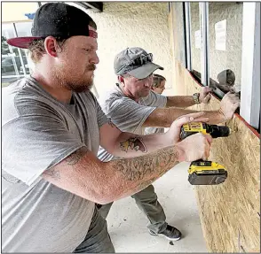  ?? AP/Rocky Mount Telegram/ALAN CAMPBELL ?? Dominic Carucci (from left), Michael Waldo and Robert McKeehan attach sheets of plywood to the front of a dress store Wednesday in Rocky Mount, N.C., about 100 miles inland.