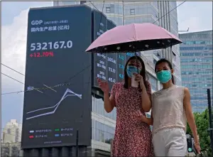  ?? (AP/Andy Wong) ?? Women walk past an electronic billboard showing China’s gross domestic product index on a commercial office building in Shanghai last month.