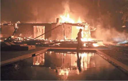  ??  ?? A firefighte­r walks by a burning home in Malibu on Friday night. California fire officials said the Woolsey fire has destroyed at least 150 homes and forced residents to evacuate the entire seaside city of Malibu.