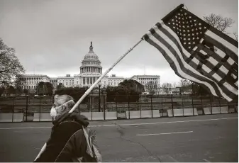  ?? John Moore / Getty Images ?? A demonstrat­or walks by as the American flag flies at half-staff at the U.S. Capitol on Friday in honor of Capitol police officer Brian Sicknick, 42, who died after clashes with a pro-Trump mob.