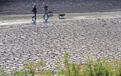  ?? JOHN LOCHER/AP ?? People walk by cracked earth at the Lake Mead National Recreation Area near Boulder City, Nev. The most intense droughts include the one in the American Southwest that has caused dangerousl­y low water levels in lakes.
