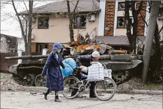  ?? Alexei Alexandrov / Associated Press ?? Local civilians walk past a tank destroyed during heavy fighting in an area controlled by Russian-backed separatist forces in Mariupol, Ukraine, on Tuesday,. Taking Mariupol would deprive Ukraine of a vital port and complete a land bridge between Russia and the Crimean Peninsula, seized from Ukraine from 2014.